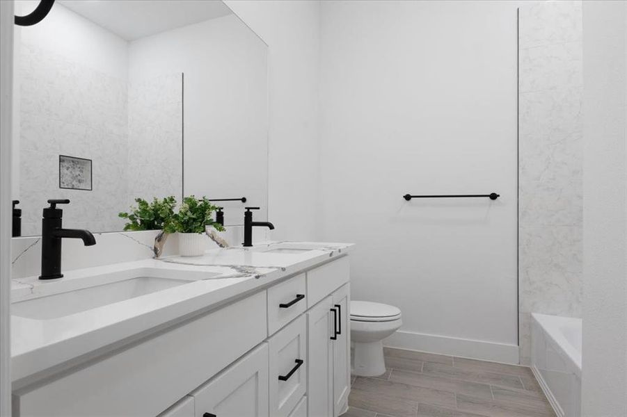 Full bath with toilet, double vanity, baseboards, and a sink