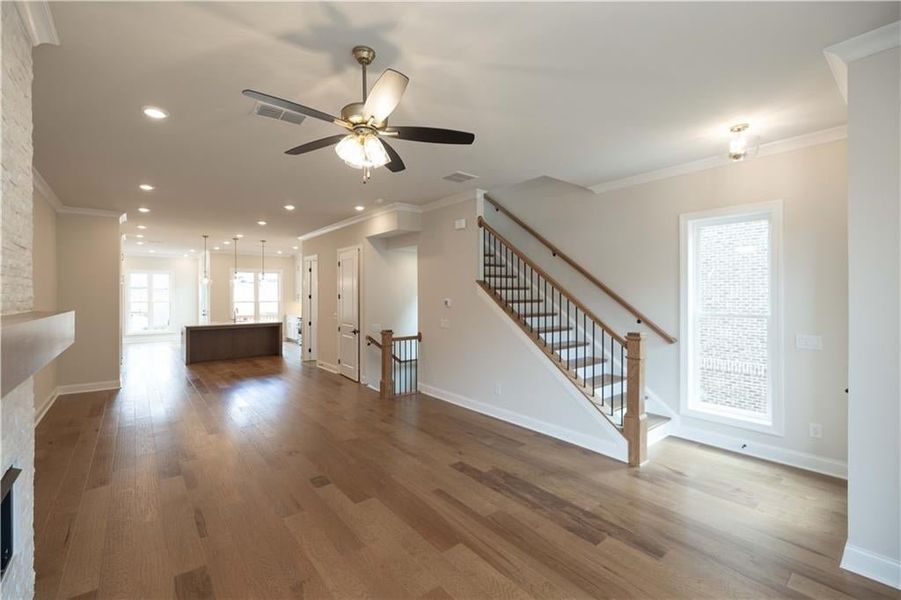 Unfurnished living room featuring hardwood / wood-style floors, a fireplace, ornamental molding, and ceiling fan