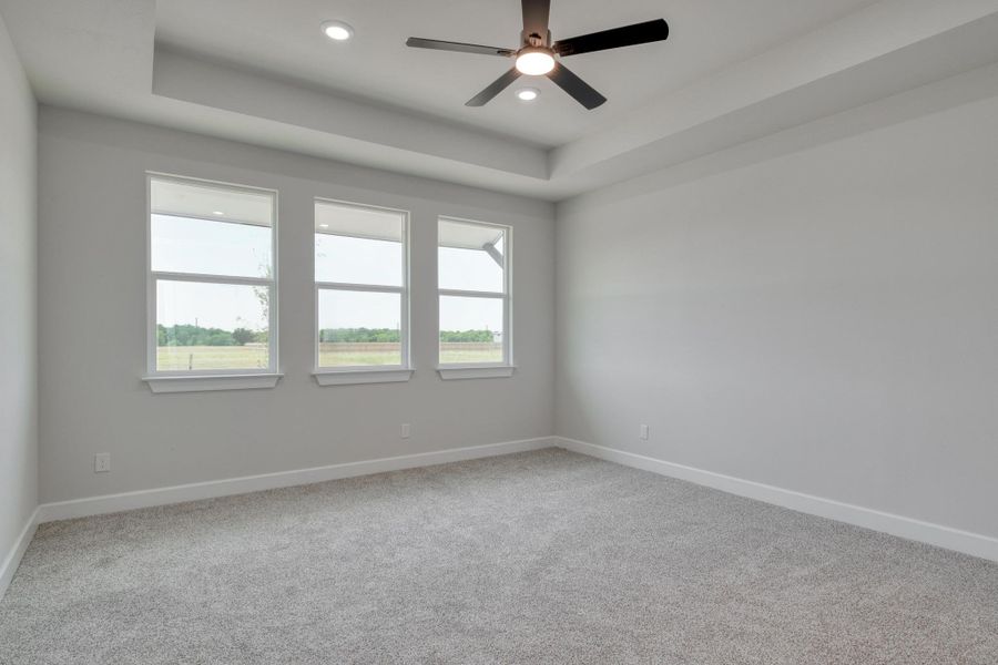 Unfurnished room with a raised ceiling, carpet, baseboards, recessed lighting, and ceiling fan
