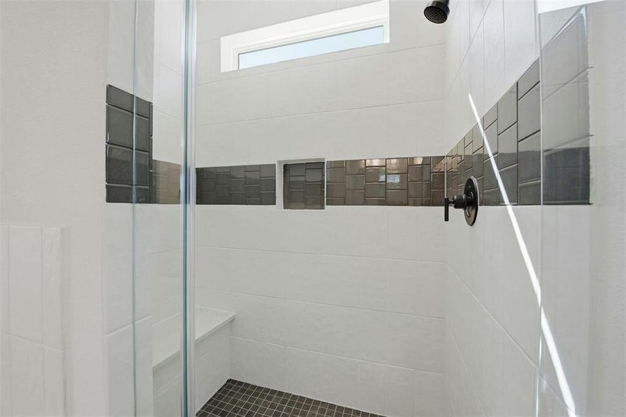 Walk-in shower featuring a fixed glass panel, white subway tile, a decorative tile accent band with two recessed niches, a built-in bench, and a dark-finish shower head and controls