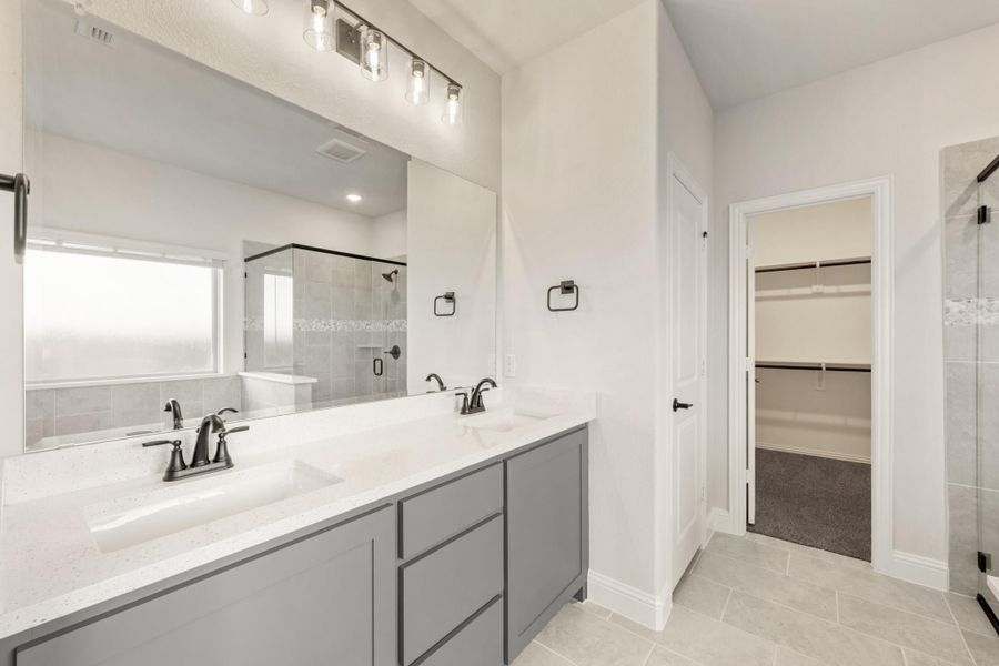 Master bathroom with double vanity, gray cabinets, glass shower, and walk-in closet entrance Master bathroom with double vanity, gray cabinets, glass shower, and walk-in closet entrance