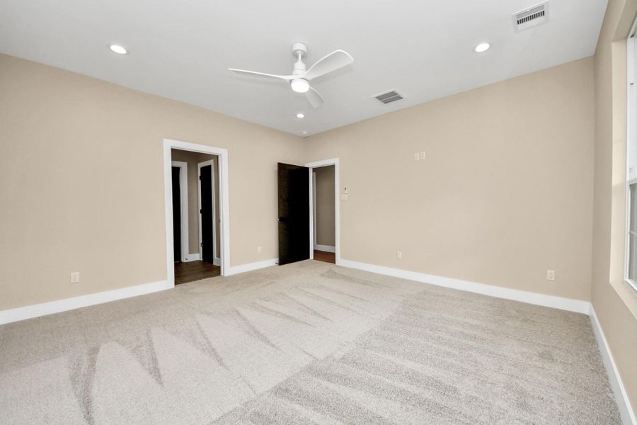 Spacious first-floor primary bedroom featuring soft carpet, warm neutral paint tones, recessed lighting, and a modern ceiling fan—creating a comfortable and relaxing retreat.