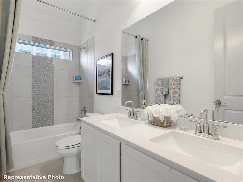 This bathroom features a double vanity with white countertops, a bathtub with a tiled surround, and a window above the bath