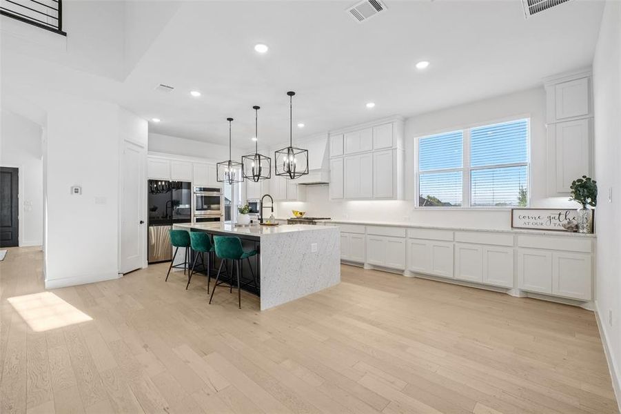 Kitchen with a kitchen bar, decorative light fixtures, an island with sink, white cabinets, and stainless steel appliances Kitchen with a kitchen bar, decorative light fixtures, an island with sink, white cabinets, and stainless steel appliances