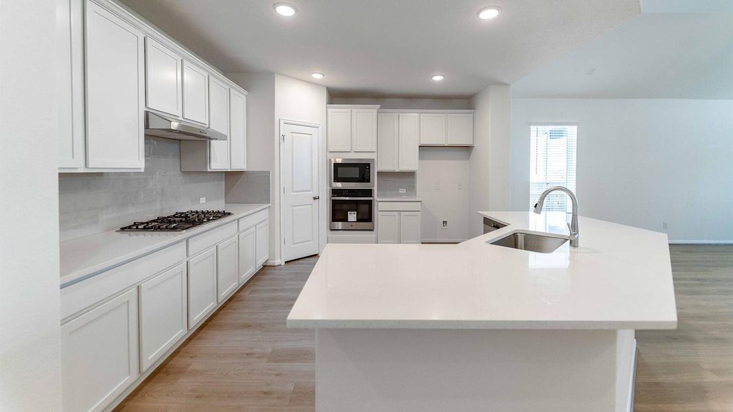 Kitchen featuring a kitchen island with sink, backsplash, stainless steel appliances, white cabinets, and light wood-style floors