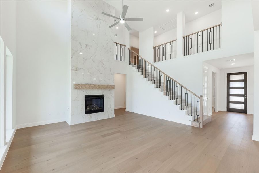 Open living room with two-story ceiling, marble fireplace wall, staircase, and light hardwood floors
