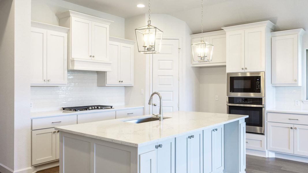 Kitchen featuring decorative backsplash, light stone countertops, appliances with stainless steel finishes, white cabinetry, and an island with sink Kitchen featuring decorative backsplash, light stone countertops, appliances with stainless steel finishes, white cabinetry, and an island with sink