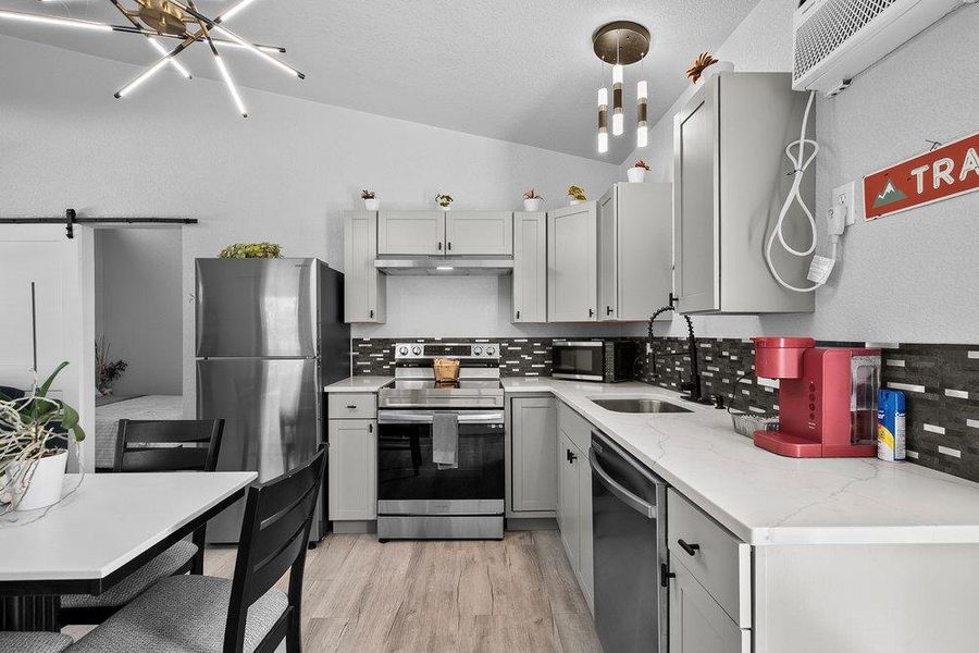 Kitchen with a barn door, stainless steel appliances, a chandelier, light wood-style floors, and decorative backsplash.