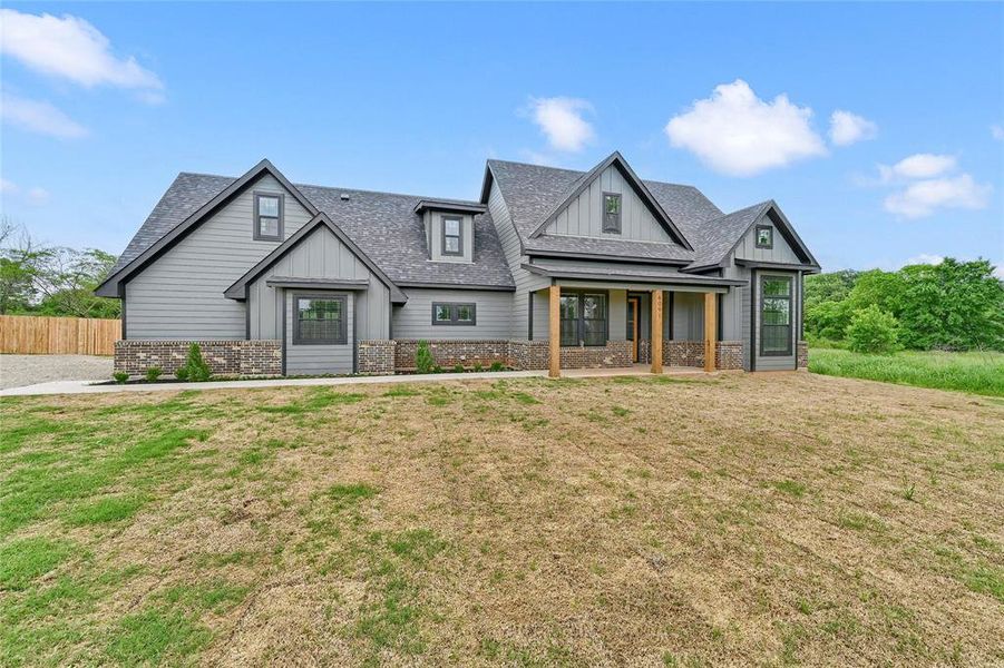 View of front of house with a front lawn, fence, roof with shingles, brick siding, and board and batten siding