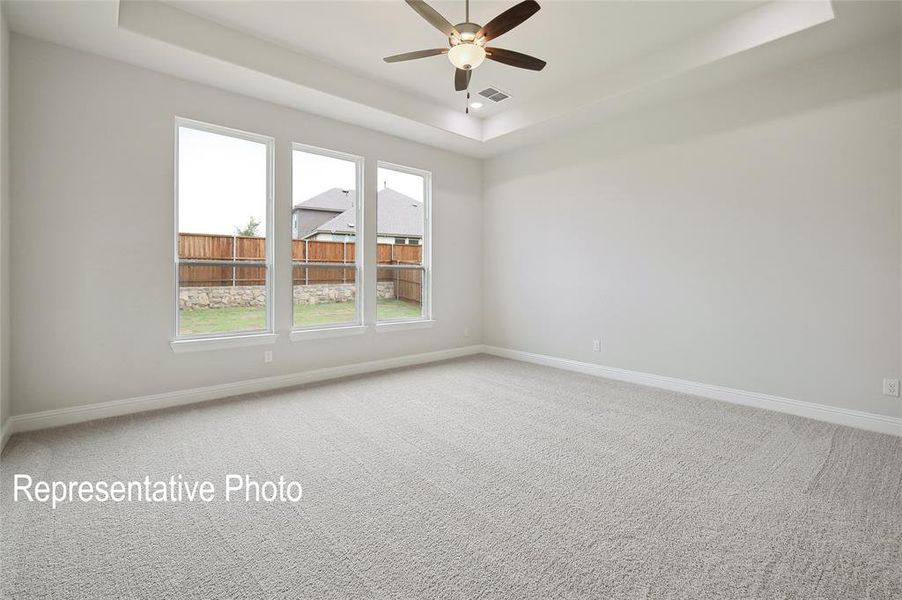 Spacious room featuring light-colored carpeting, three tall windows, a tray ceiling, and a ceiling fan with integrated lighting