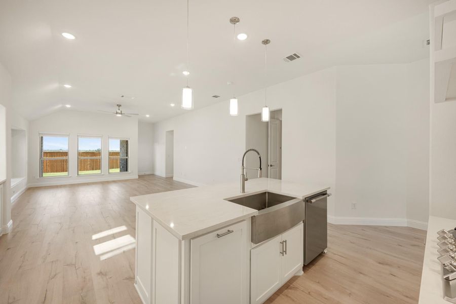 Kitchen island with farmhouse sink, white cabinets, and pendant lights open to living area with vaulted ceiling
