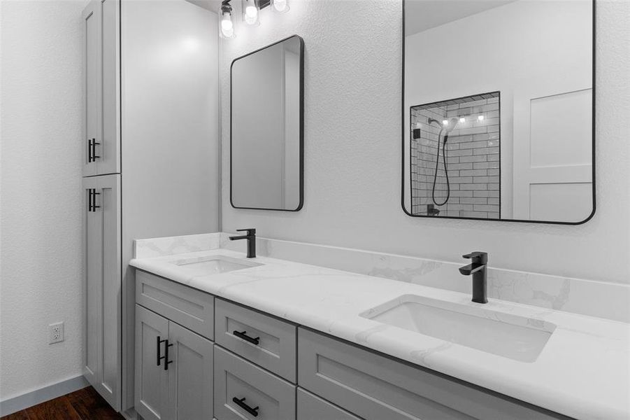 Bathroom with double vanity, a textured wall, tiled shower, and dark wood-style flooring