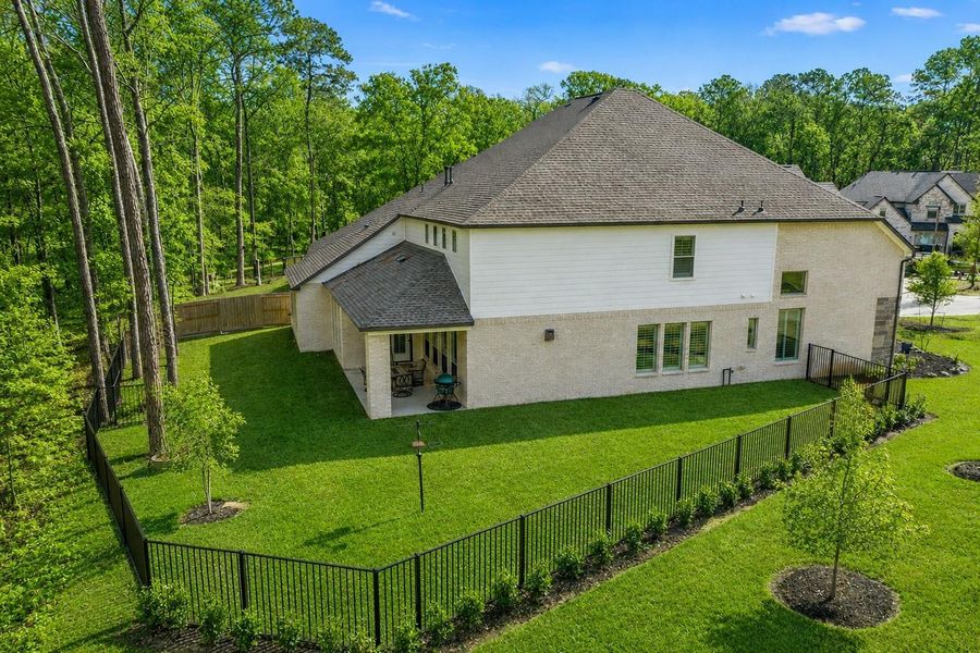 This photo showcases a spacious two-story home with a fenced backyard, bordered by a serene wooded area. The property features a well-maintained lawn and a covered patio, perfect for outdoor relaxation. Ideal for those seeking privacy and a connection to nature.