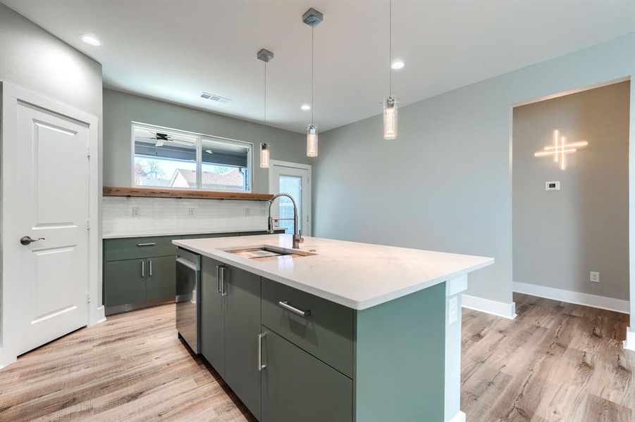 Kitchen with hanging light fixtures, backsplash, a kitchen island with sink, and sink