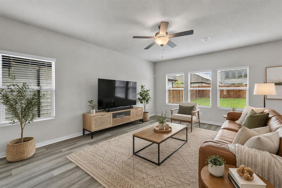 *Virtually Staged* Spacious living area featuring wood-finish flooring, a ceiling fan with integrated lighting, multiple windows with blinds, and light-toned wall finishes