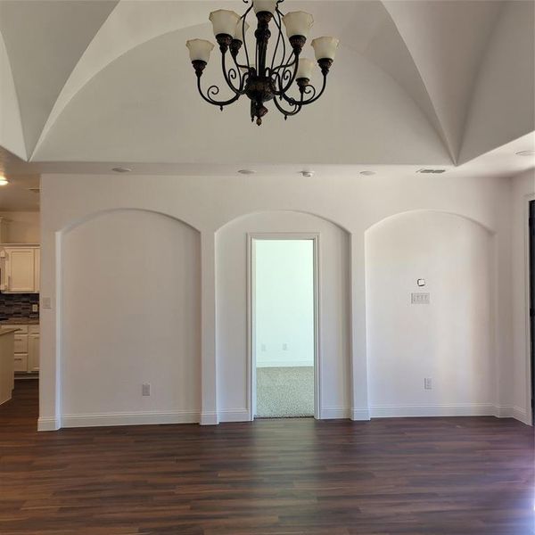 Empty room featuring a chandelier, dark wood-type flooring, and vaulted ceiling