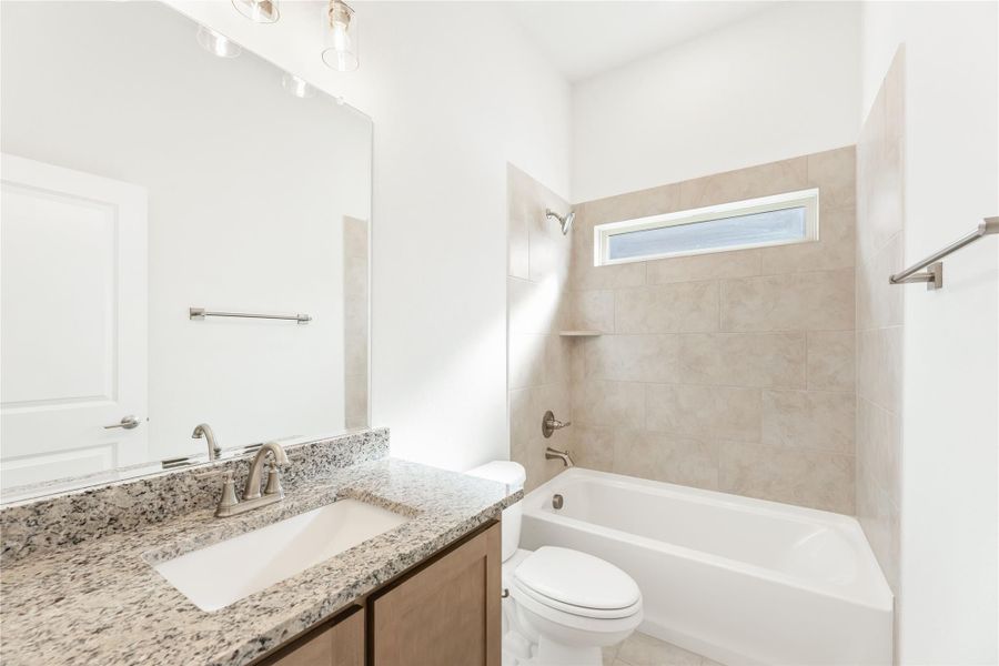 Bathroom with granite countertop vanity, soaking tub, and beige tile surround with small window Bathroom with granite countertop vanity, soaking tub, and beige tile surround with small window