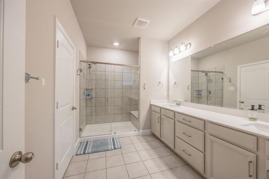 Primary bathroom with a quartz dual sink vanity countertop, white cabintery with door handles and a walk in shower with bench seat - View