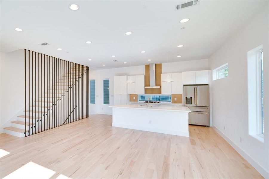 Kitchen with wall chimney range hood, an island with sink, pendant lighting, high quality fridge, and white cabinetry