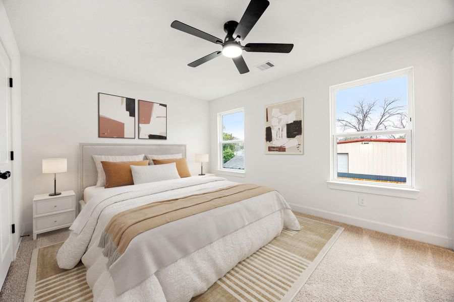 This bright and inviting secondary bedroom features soft neutral tones, plush carpeting, a ceiling fan, and ample natural light, creating a comfortable and versatile space ideal for guests, a home office, or additional living needs.