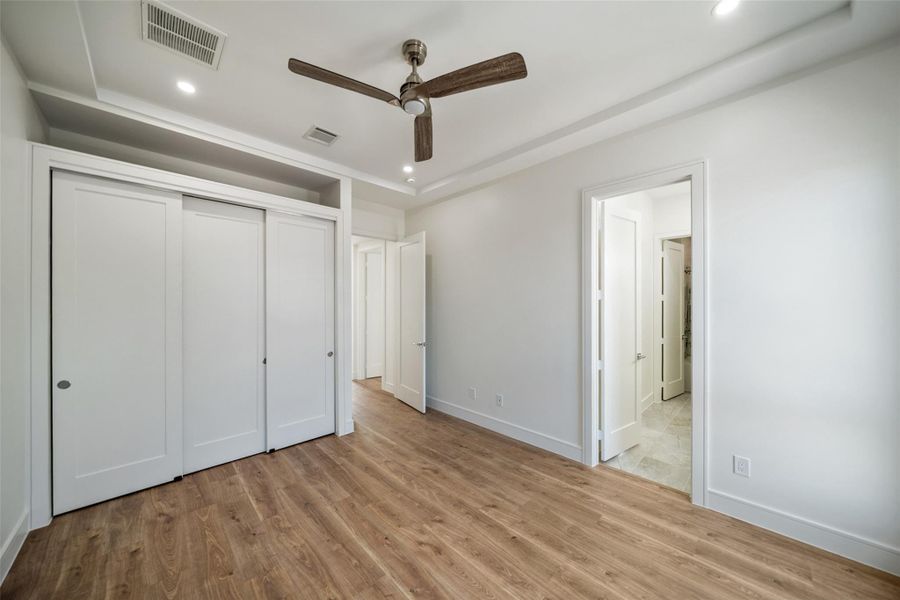 Upstairs Secondary bedroom features wood flooring, a ceiling fan, and a built-in closet with sliding doors. It has recessed lighting and a neutral color scheme, offering a modern and airy feel.