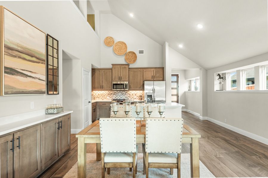 Open dining area with wood table and white chairs flowing into kitchen with vaulted ceiling and hardwood floors
