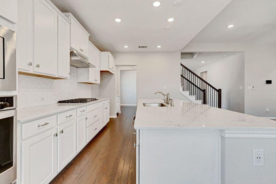 Kitchen featuring white cabinetry, light stone counters, dark wood-type flooring, recessed lighting, and tasteful backsplash Kitchen featuring white cabinetry, light stone counters, dark wood-type flooring, recessed lighting, and tasteful backsplash