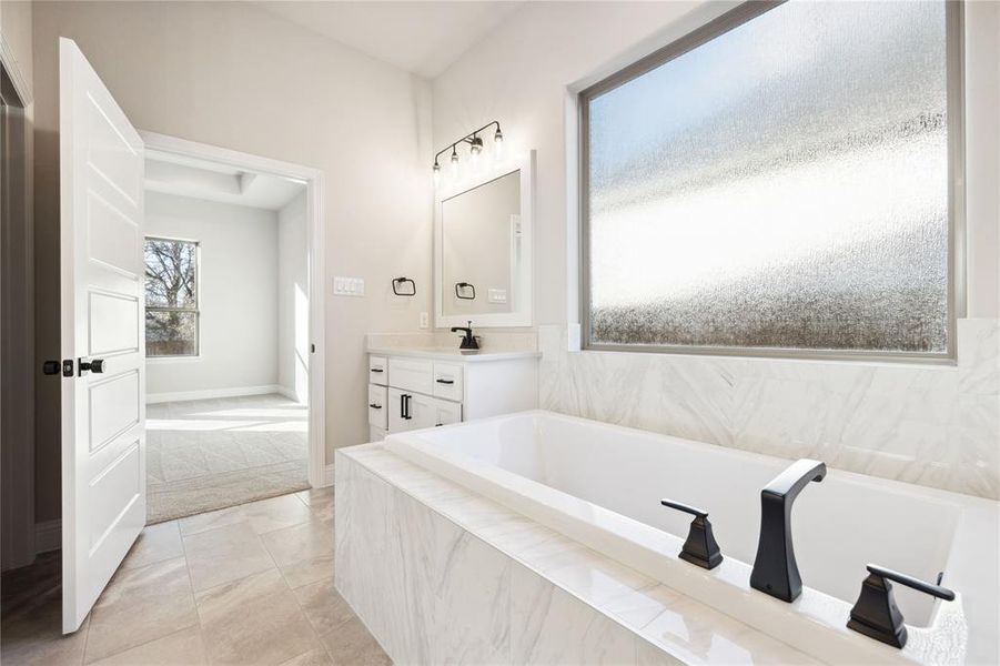 Bathroom featuring tile patterned floors, vanity, and tiled bath