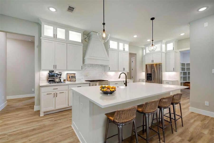 Kitchen features include formica countertops paired with a coordinating stone backsplash, stainless steel appliances, crisp white cabinets with updated hardware, under cabinet lighting, recessed lighting, and a sprawling island with breakfast bar seating.