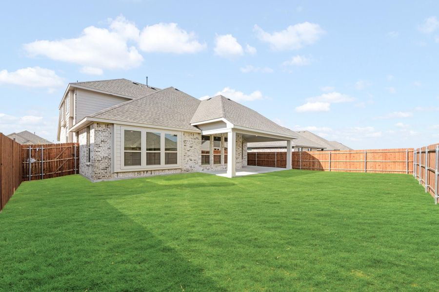 Brick home rear view with covered patio, large green lawn, and wood privacy fence