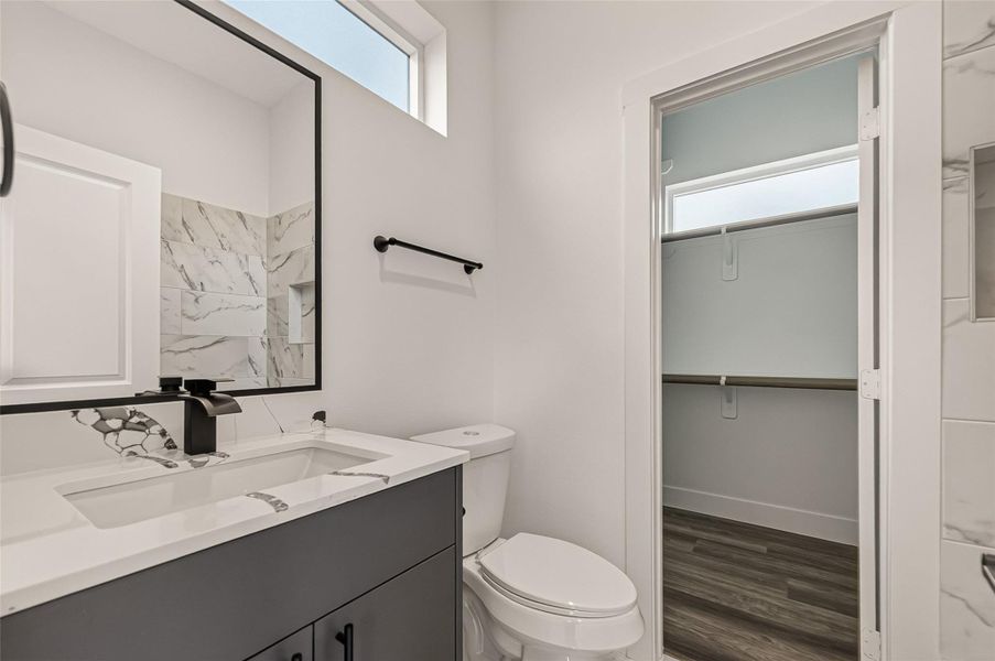 Modern bathroom with a sleek design featuring a marble countertop, rectangular sink, and black fixtures. Includes a large mirror, a window for natural light, and a doorway leading to a spacious closet with built-in shelving. Modern bathroom with a sleek design featuring a marble countertop, rectangular sink, and black fixtures. Includes a large mirror, a window for natural light, and a doorway leading to a spacious closet with built-in shelving.