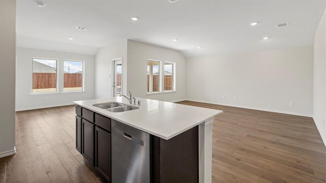 Kitchen island with a double basin stainless steel sink, a stainless steel dishwasher, white countertop, and dark wood-finish cabinetry