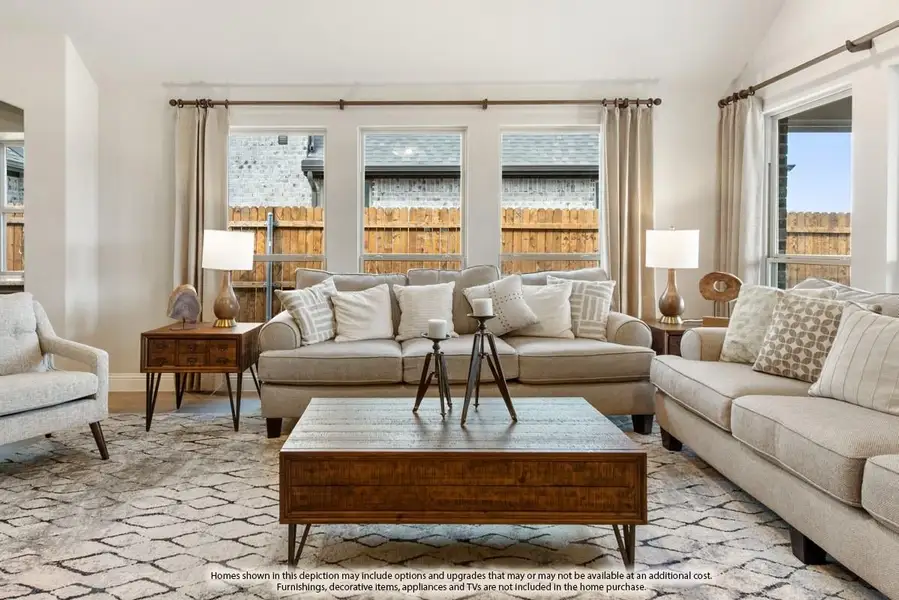 Living room with beige sofas, wood coffee table, patterned area rug, and large windows with neutral curtains