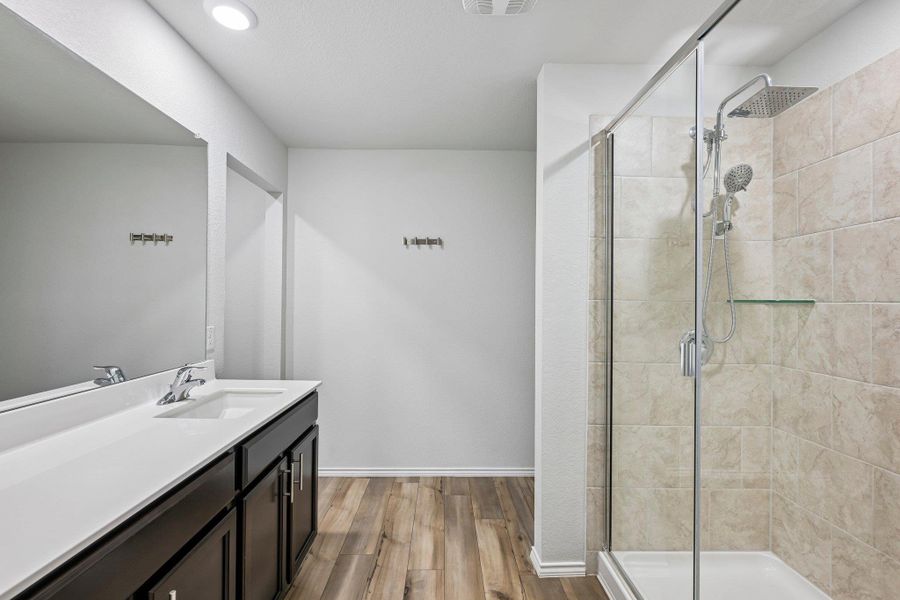 Full bathroom featuring a frameless glass shower enclosure, a rain showerhead, a single vanity with a white countertop, and wood-finish flooring