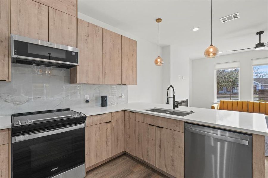 Kitchen with light brown cabinets, kitchen peninsula, sink, and appliances with stainless steel finishes