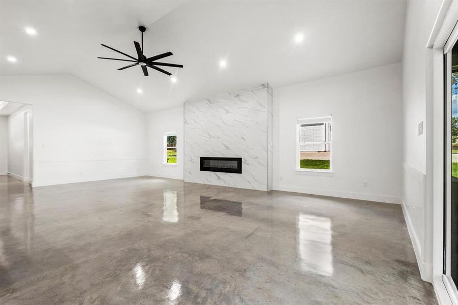 Unfurnished living room featuring a premium fireplace, finished concrete floors, a ceiling fan, recessed lighting, and high vaulted ceiling