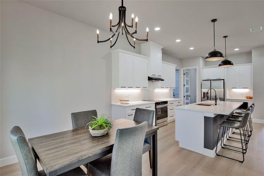 Kitchen featuring a breakfast bar area, white cabinets, an island with sink, stainless steel appliances, and recessed lighting Kitchen featuring a breakfast bar area, white cabinets, an island with sink, stainless steel appliances, and recessed lighting