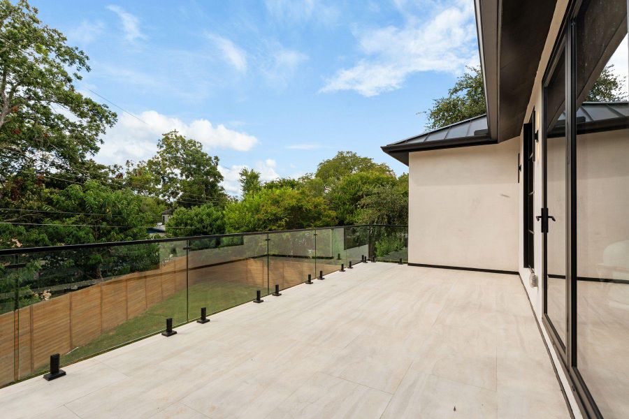 An upper-level tiled terrace is enclosed by glass railings overlooking mature green trees.