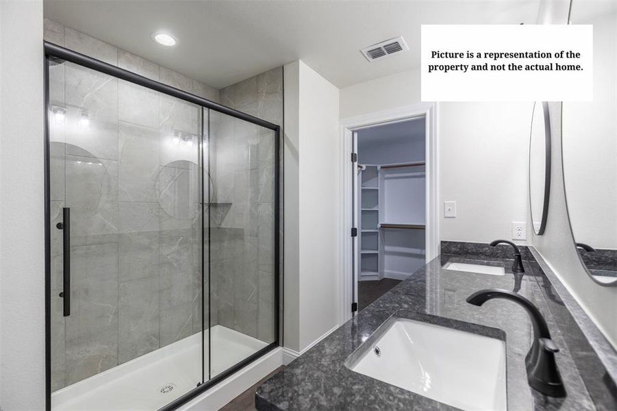 Modern bathroom featuring a double vanity with dark countertops and integrated sinks, matte black fixtures, an expansive glass-enclosed shower with tile surround, and recessed lighting