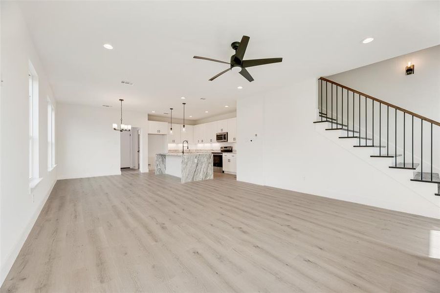 Unfurnished living room featuring a chandelier, light wood-style floors, recessed lighting, stairway, and ceiling fan