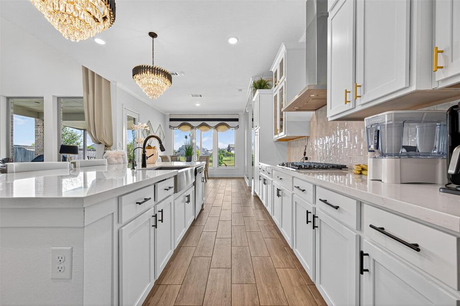 This kitchen features a spacious, open layout with white cabinetry, modern appliances, and elegant lighting fixtures. The large island offers ample counter space and a sink, while wood-look flooring adds warmth. Expansive windows provide plenty of natural light and scenic views. This kitchen features a spacious, open layout with white cabinetry, modern appliances, and elegant lighting fixtures. The large island offers ample counter space and a sink, while wood-look flooring adds warmth. Expansive windows provide plenty of natural light and scenic views.