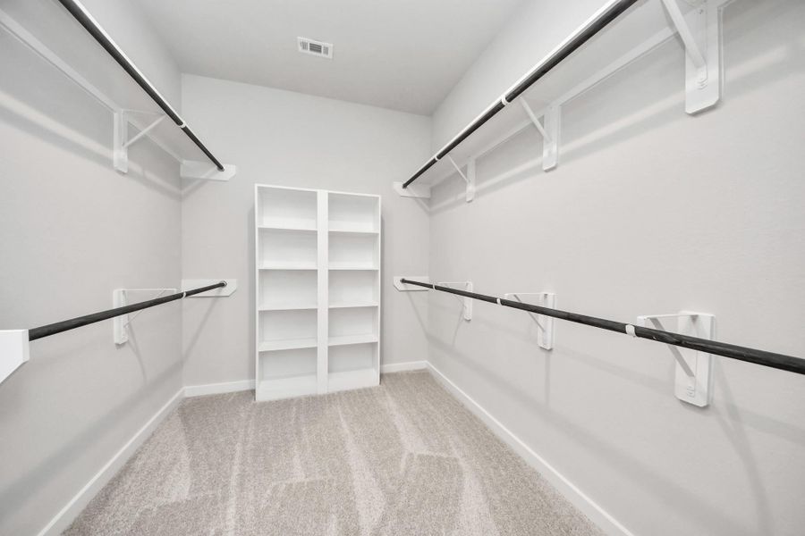 Walk-in closet that epitomizes luxury and practicality. This generously sized space features built-in shelving, offering abundant room for impeccable organization. High ceilings and recessed lighting create a bright and welcoming ambiance. Sample photo of completed home with similar floor plan. Actual colors and selections may vary.