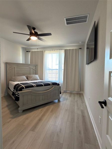 Bedroom featuring light wood-finish flooring, a ceiling fan with integrated lighting, and multiple windows with curtain rods