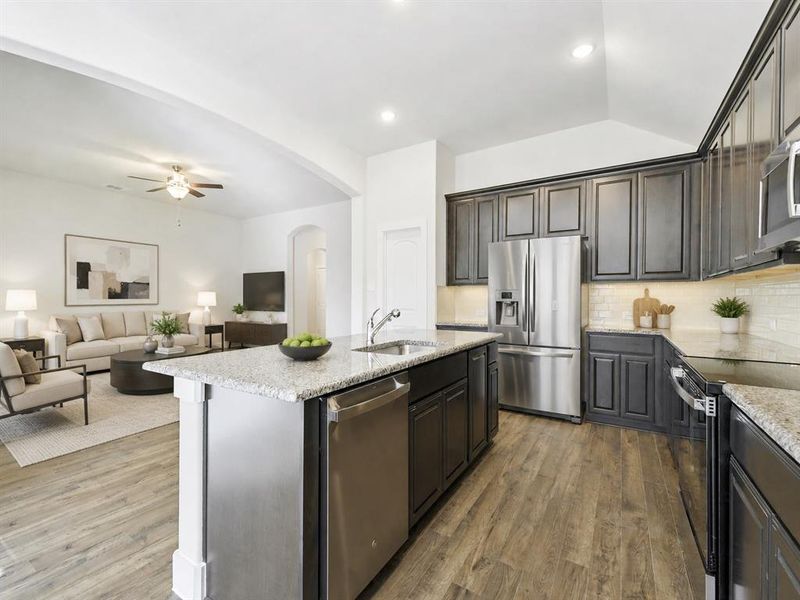 Kitchen featuring a central island with an integrated sink and dishwasher, wood-finish flooring, dark cabinetry, and light-toned countertops