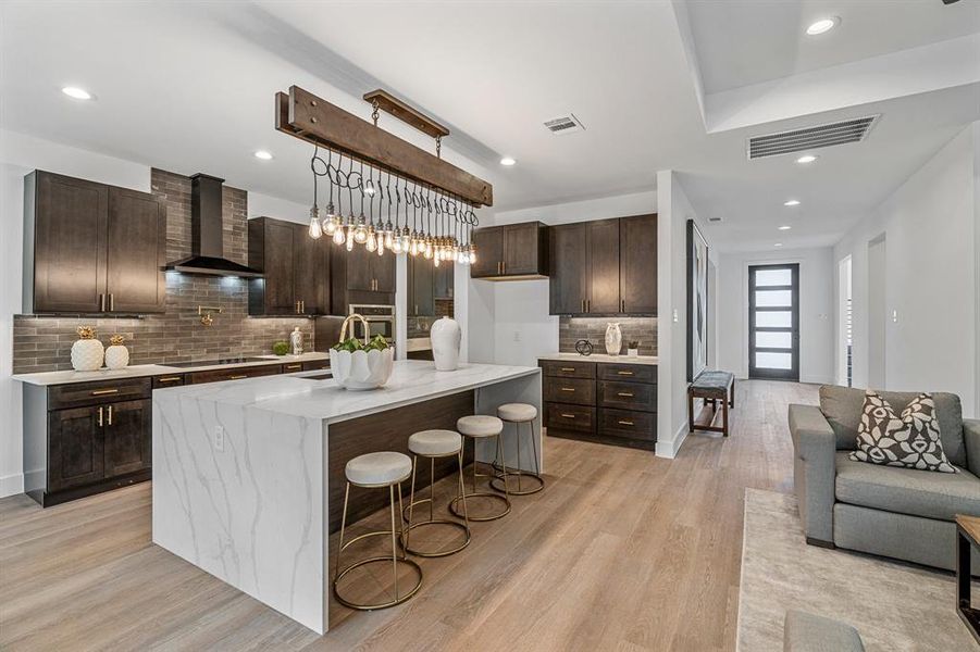 Kitchen featuring a center island with sink, wall chimney range hood, light hardwood / wood-style floors, and tasteful backsplash