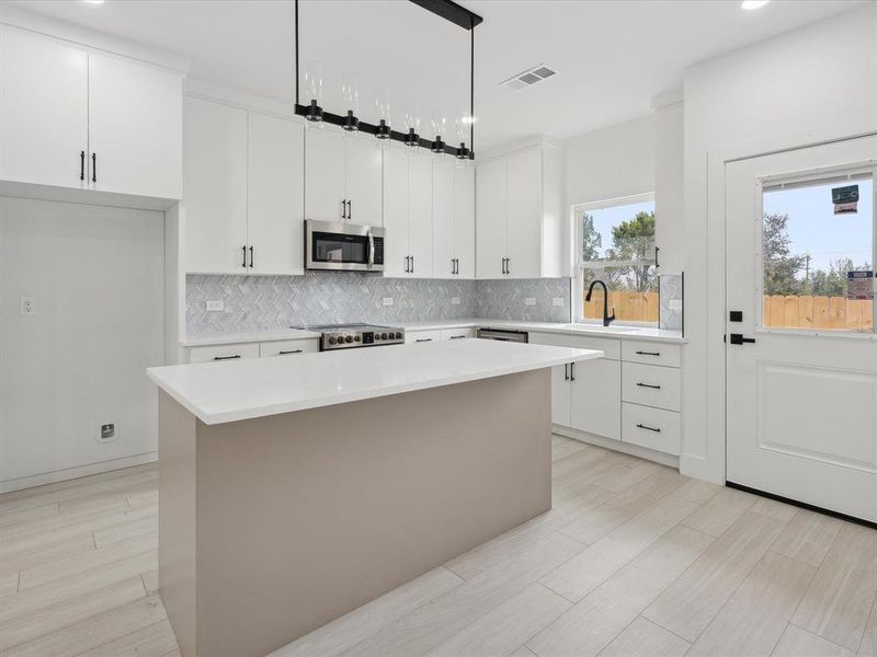 Kitchen featuring white cabinetry, sink, a center island, pendant lighting, and appliances with stainless steel finishes