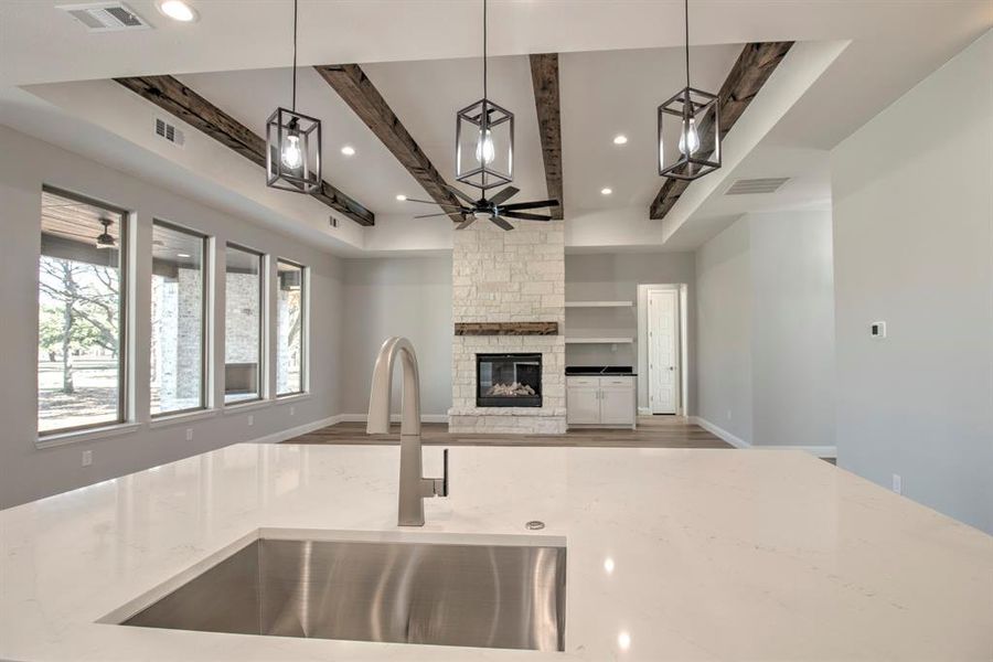 Kitchen featuring light stone countertops, sink, a stone fireplace, beamed ceiling, and pendant lighting