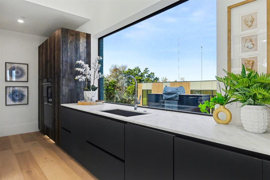 Kitchen with modern cabinets, light stone counters, light wood finished floors, and dark cabinetry