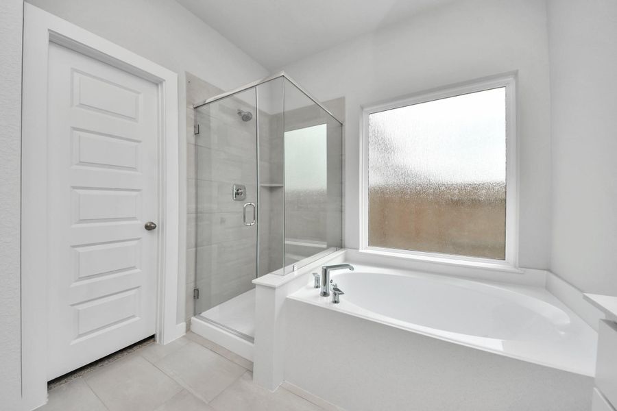 Indulge in a spa-like retreat within the confines of this primary bathroom. Delight in a spacious walk-in shower enveloped in stylish tile surround, unwind in a separate garden tub adorned with custom detailing. Sample photo of completed home with similar floor plan. Actual colors and selections may vary.