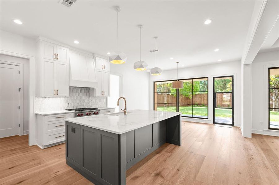Kitchen with white cabinetry, pendant lighting, light stone countertops, light wood finished floors, and decorative backsplash Kitchen with white cabinetry, pendant lighting, light stone countertops, light wood finished floors, and decorative backsplash